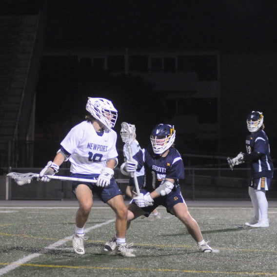 Newport Harbor Lacrosse player with a ball, defended by two opponents